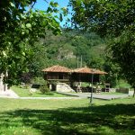 Vista de la zona verde de los apartamentos donde podemos ver dos horreos conectados entre si, con árboles a su alrededor, al fondo se ve una ladera con árboles