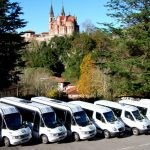 Vista de la flota de furgonetas y mini buses de la empresa «Taxitur» aparcados en batería a la espera de pasajeros. Al fondo vemos la parte trasera de la Basílica de Covadonga.