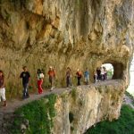 Un grupo de personas camina en fila indica por un tramo de la Ruta del Cares, saliendo de un túnel y siguiendo el sinuoso recorrido de la ruta