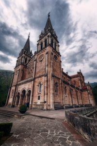 Vista fronto lateral de la Basílica de Covadonga, en plano contrapicado, enmarcada por un cielo cubierto de nubes