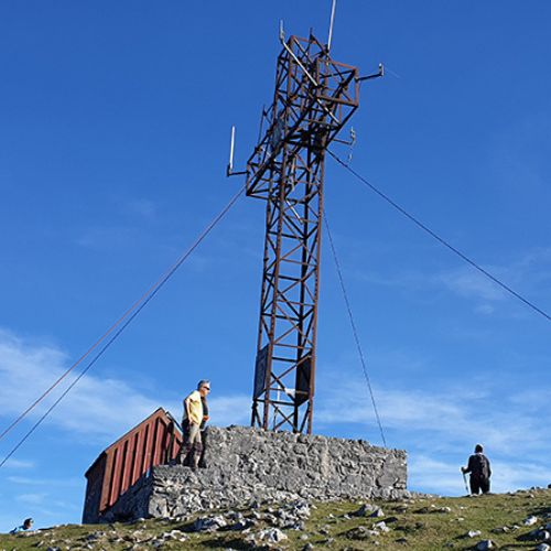 Una cruz metálica formada por viguetas y sujeta al suelo por cables, con unos cimientos de piedra, en lo alto del Pico Pienzu