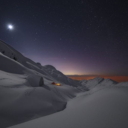 Vista nocturna de Vegarredonda cubierta por la nieve, donde se ven rastros de pisadas alrededor del refugio de las tiendas de campaña