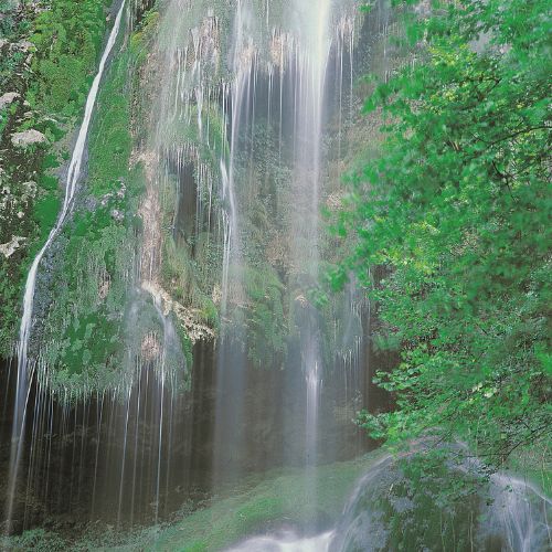 Vista de la cascada de Aguasalíu, en un toma de larga duración para que el agua forme una cortina, que cae sobre rocas cubiertas de musgo
